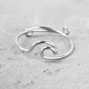 May include: A silver ring with a wave design. The ring is made of a single piece of wire that is bent into the shape of a wave.