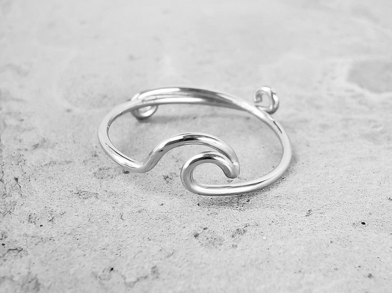 May include: A silver ring with a wave design. The ring is made of a single piece of wire that is bent into the shape of a wave.