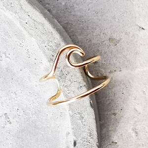 May include: A gold-toned wave ring made of wire. The ring is open and adjustable.