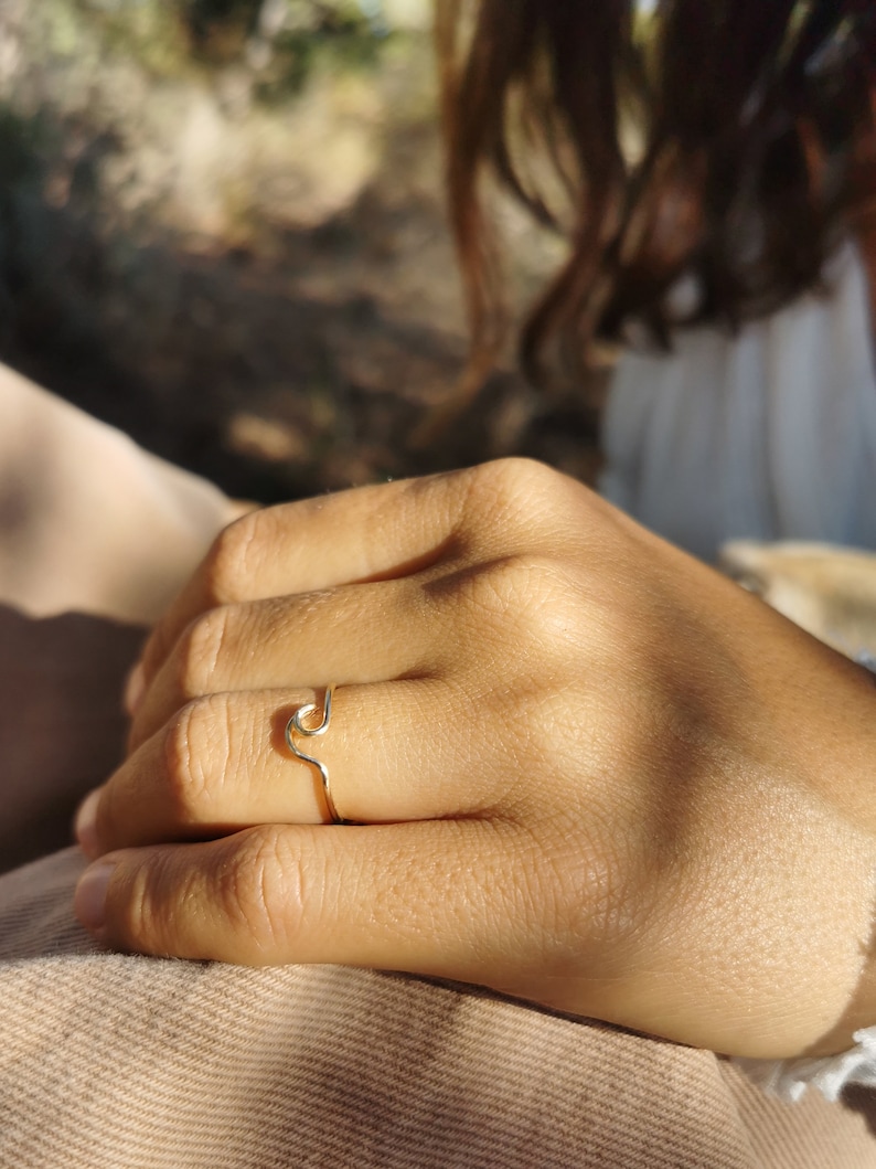 May include: A gold ring with a wave design. The ring is worn on a person's finger.