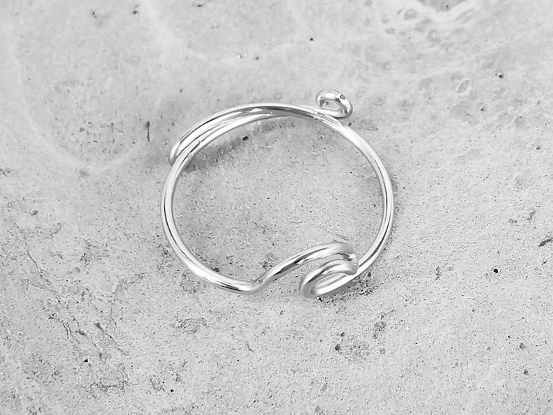 May include: A silver ring with a twisted wire design. The ring has a small loop at the top for attaching a charm.