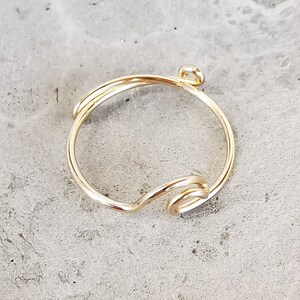 May include: A gold-toned ring with a simple, twisted design. The ring has a small loop at the top, suggesting it is a charm or pendant.