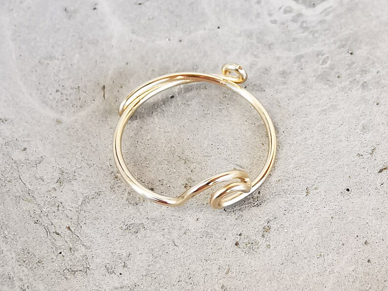 May include: A gold-toned ring with a simple, twisted design. The ring has a small loop at the top, suggesting it is a charm or pendant.