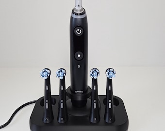 Może przedstawiać: Czarna rączka szczoteczki elektrycznej Oral-B iO z przyciskiem zasilania i wyświetlaczem, umieszczona na czarnej ładowarce. Cztery czarne końcówki wymienne z niebiesko-białym włosiem są umieszczone w otworach podstawy.