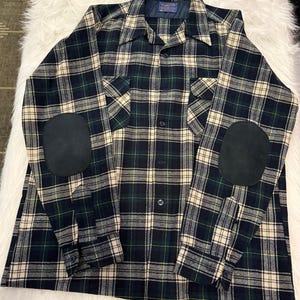May include: A long-sleeve button-down shirt featuring a dark green, navy blue, and cream plaid pattern. The shirt includes a pointed collar, two chest pockets with flaps, and solid black oval-shaped elbow patches on each sleeve.