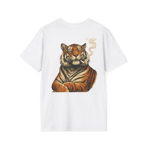 Peut inclure: T-shirt blanc avec une illustration détaillée d'un tigre fumant une cigarette. Le tigre a des rayures orange et noires et une expression détendue. La fumée s'élève de la cigarette. Le t-shirt est de style col rond classique.