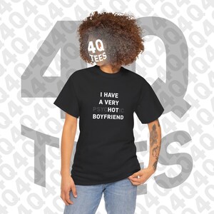 May include: A black short-sleeve t-shirt featuring the white text I HAVE A VERY PSYCHOTIC HOT BOYFRIEND, with the word PSYCHOTIC partially obscured by a greyed-out effect. The shirt has a crew neckline and a standard fit, worn with blue denim jeans.
