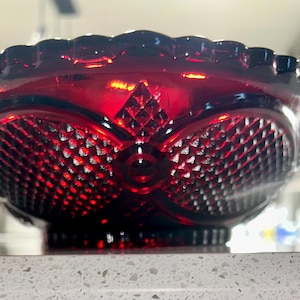 May include: A deep red glass bowl featuring a prominent diamond point pattern across its exterior surface. The bowl has a scalloped rim and a circular base, with the pressed glass design creating a textured appearance that catches the light.