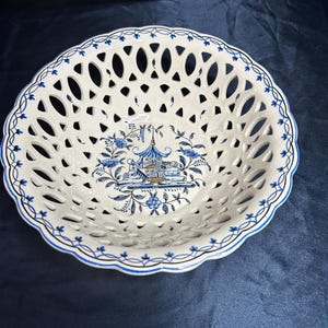 May include: White ceramic openwork bowl with a blue and white floral design. The bowl has a scalloped edge with blue trim and a central illustration of a pagoda and flowers. The bowl is likely for decorative or serving purposes.