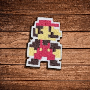 May include: A pixelated embroidered patch featuring a character with a red hat, red overalls, and yellow skin tones. The design is rendered in a blocky, 8-bit style with a white border, showcasing a classic video game aesthetic in a flat, stitched format.