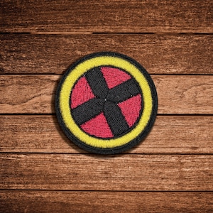 May include: A circular embroidered patch featuring a vibrant red center divided by a thick black X-shaped cross, all enclosed within a bright yellow border and a thin black outer edge, creating a bold and high-contrast graphic design element.