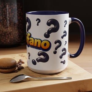 May include: A white ceramic mug with a dark blue interior and handle. The exterior features a repeating pattern of black question marks and the word "ifano" printed in a bold, yellow-to-orange gradient font with a dark blue outline.