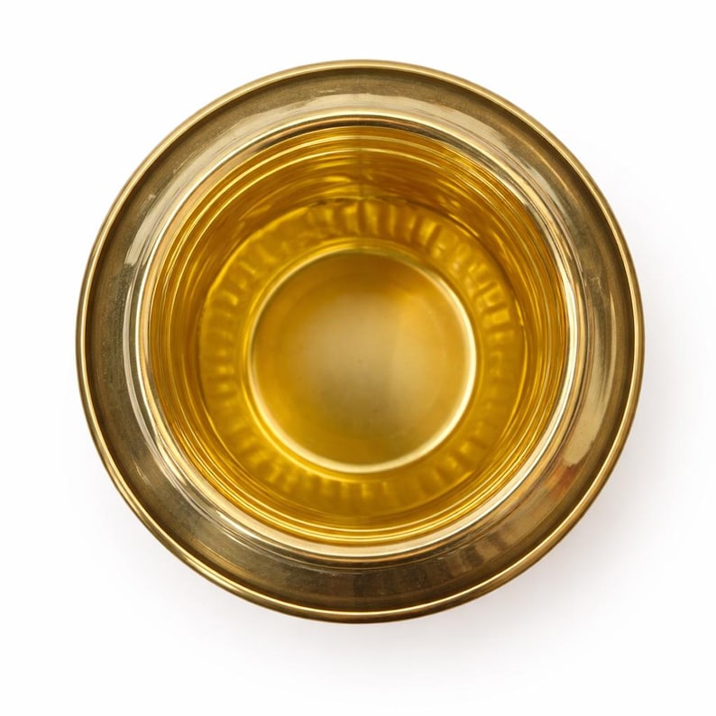 May include: Overhead view of a gold-colored metal bowl. The bowl has a wide, flat rim and a rounded interior. The interior has a series of concentric rings. The bowl is set against a white background.