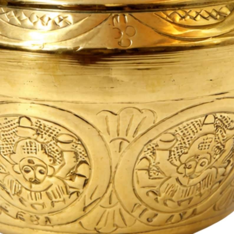 May include: Close-up of a gold-colored metal bowl with intricate engraved designs. The bowl features detailed patterns of figures and floral motifs. The upper rim has a decorative border, and the overall design suggests a vintage or antique aesthetic.