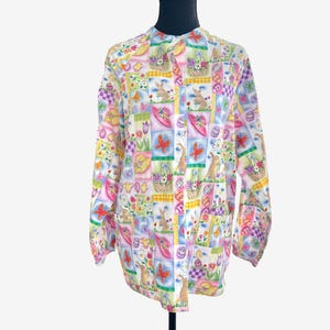 May include: A long-sleeved button-down shirt featuring a colorful patchwork print of Easter-themed imagery, including rabbits, decorated eggs, flower baskets, butterflies, and sun hats in shades of pink, yellow, green, blue, and purple.