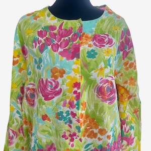 May include: A long-sleeved button-down shirt featuring a vibrant floral pattern with shades of bright pink, lime green, orange, and yellow. The garment has a round neckline and white buttons running down the center front, set against a white background.