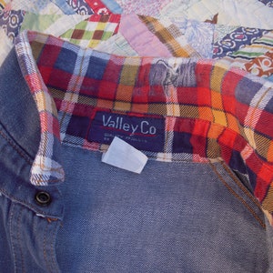 May include: A blue denim shirt with a red, yellow, and black plaid flannel lining. The shirt has a button closure and a label that reads "ValleyCo Quality Products".