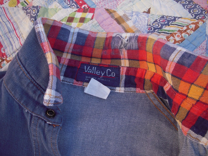 May include: A blue denim shirt with a red, yellow, and black plaid flannel lining. The shirt has a button closure and a label that reads "ValleyCo Quality Products".