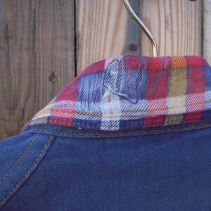 May include: A blue denim jacket with a red, white, and yellow plaid flannel collar.