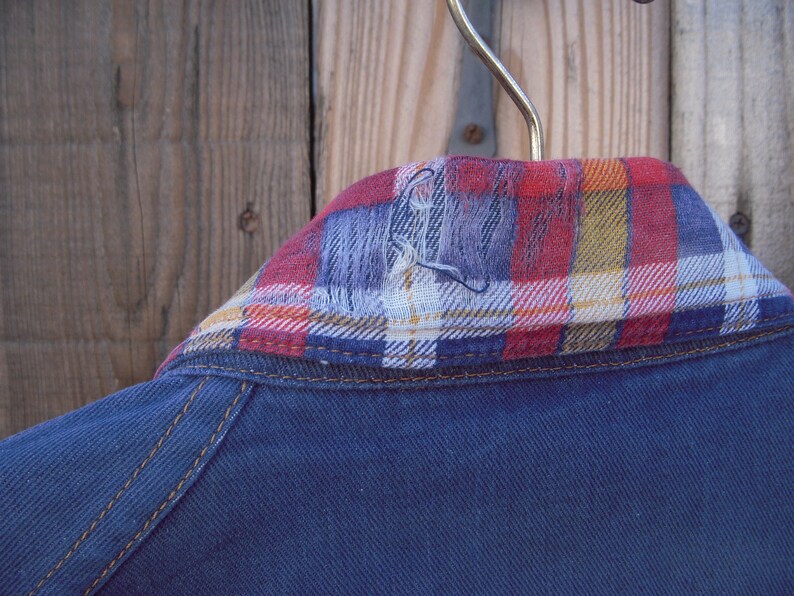 May include: A blue denim jacket with a red, white, and yellow plaid flannel collar.