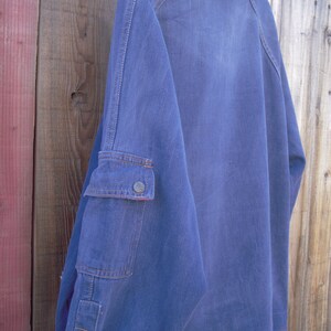 May include: A blue denim shirt with a single button on the left cuff and a patch pocket on the right sleeve.