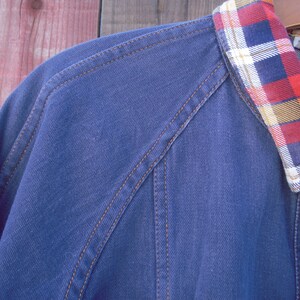 May include: A blue denim jacket with a plaid flannel collar. The jacket has brown stitching and a button closure.