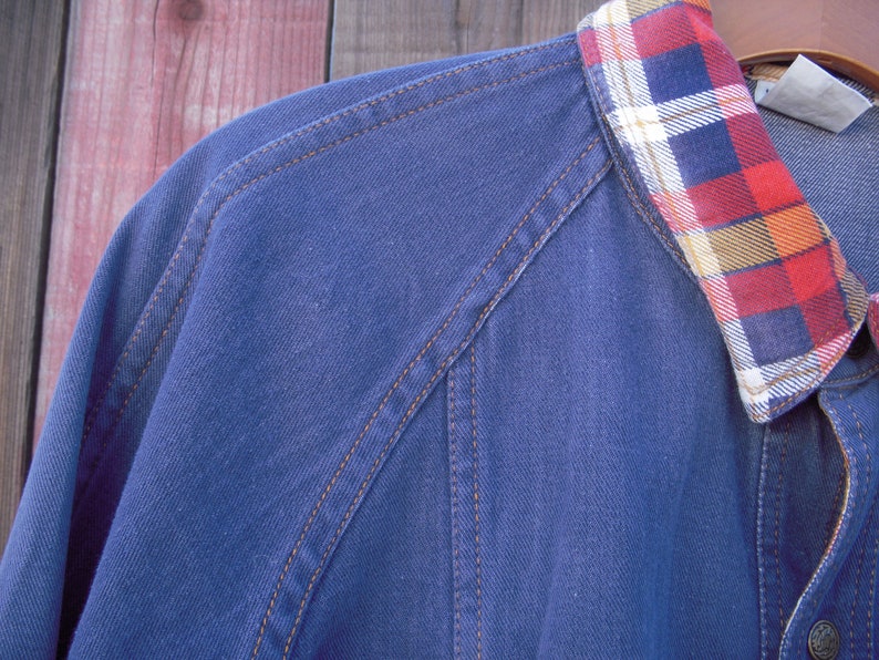 May include: A blue denim jacket with a plaid flannel collar. The jacket has brown stitching and a button closure.