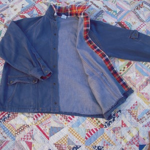 May include: A blue denim jacket with a plaid flannel lining. The jacket has a button-up front, two pockets, and long sleeves.