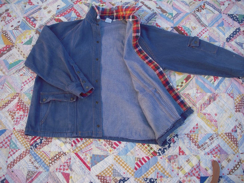 May include: A blue denim jacket with a plaid flannel lining. The jacket has a button-up front, two pockets, and long sleeves.