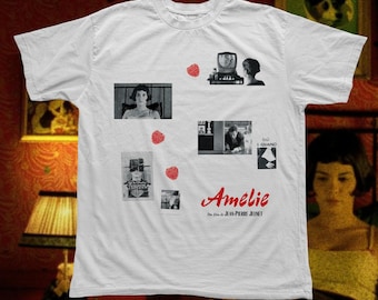 May include: A white short-sleeve t-shirt featuring multiple black and white film stills from the movie Amélie, interspersed with small red raspberry graphics. The text Amélie and Un film de JEAN-PIERRE JEUNET is printed in red.