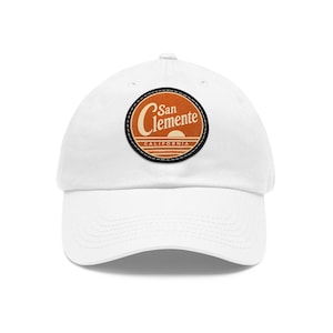 May include: A white baseball cap featuring a circular patch on the front. The patch has a dark border and an orange background with a sunset graphic, horizontal lines, and the text San Clemente California written in a stylized white font.