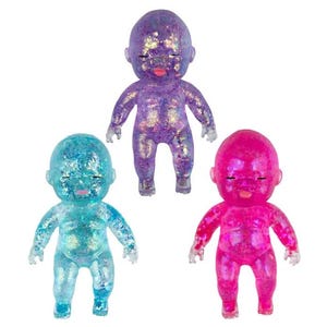 May include: Three small baby dolls with translucent bodies filled with glitter. One doll is purple, one is bright blue, and one is hot pink. Each doll features closed eyes, a small pink mouth, and a smooth, rounded head and body shape.