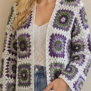 May include: A long-sleeved cardigan made of crocheted granny squares in shades of purple, green, and white. The garment features an open front design with a white border, long sleeves, and two front pockets, constructed from joined floral motifs.