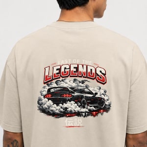 May include: A beige t-shirt featuring a graphic on the back of a black sports car surrounded by white tire smoke. Above the car, the text reads "LAST OF THE LEGENDS" in red and white. Below the car, the Japanese kanji for legend is printed in red.