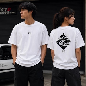 Könnte beinhalten: Ein weißes Kurzarm-T-Shirt mit einem kleinen schwarzen japanischen Schriftzeichen auf der Brust. Die Rückseite zeigt eine große, rautenförmige schwarze Grafik einer Bergstraße mit einem driftenden Auto, einem Berg und einem Schriftzeichen.