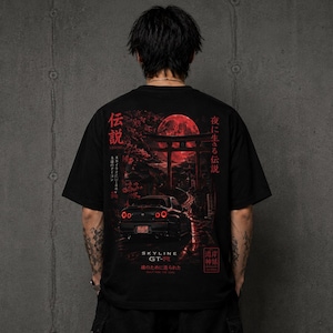 May include: Black t-shirt with a red graphic depicting a car, a full moon, and Japanese text. The design includes the text "SKYLINE GT-" and other Japanese characters. The shirt is a crew neck.