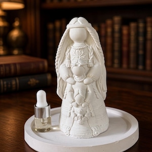May include: A white matte figurine depicting a stylized figure with braided hair and a long gown, standing on a circular white tray next to a small glass bottle with a white dropper cap. The figurine features intricate embossed patterns.