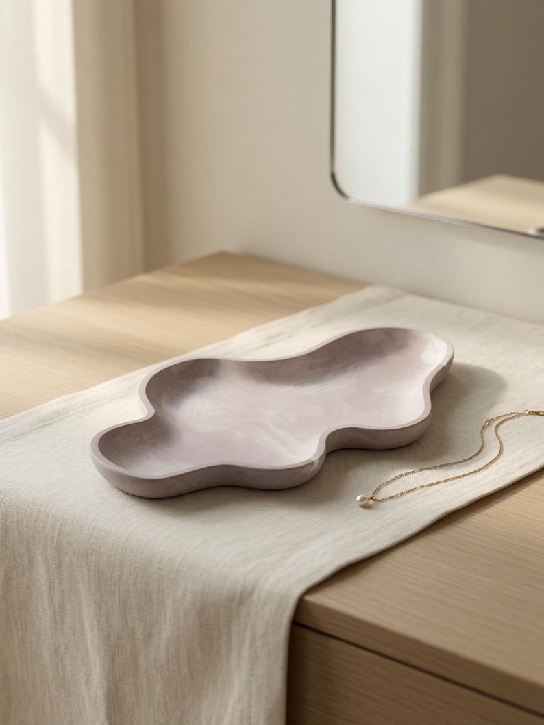 May include: A pale lavender, cloud-shaped decorative tray with a smooth, matte finish and undulating, organic edges. The tray features a shallow, recessed basin and a solid, continuous form, presented as a singular piece for holding small items.