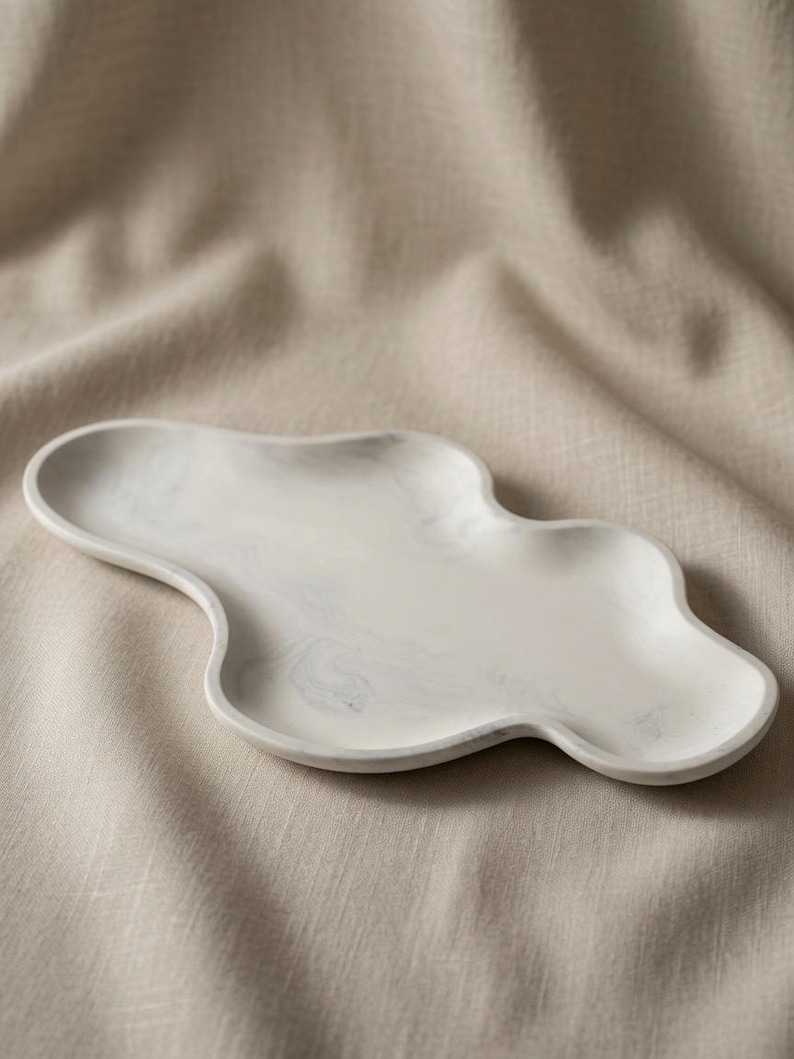 May include: An oblong, cloud-shaped tray featuring a white base with subtle, swirling gray marble-like patterns. The tray has a smooth, raised edge and an irregular, organic perimeter, presenting a flat, shallow surface for holding small items.