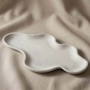May include: An oblong, cloud-shaped tray featuring a white base with subtle, swirling gray marble-like patterns. The tray has a smooth, raised edge and an irregular, organic perimeter, presenting a flat, shallow surface for holding small items.