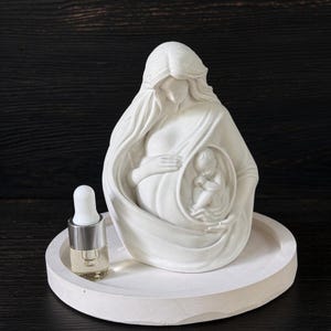 May include: A white matte sculpture of a pregnant figure with a visible fetus in the womb, placed on a circular white tray next to a small glass dropper bottle with a white cap and clear liquid inside, all featuring a smooth finish.