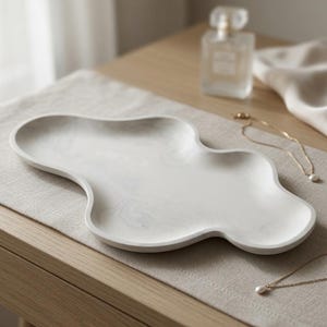 May include: A white tray with a smooth, marbled gray pattern and an irregular, cloud-like organic shape. The tray features a shallow basin with raised edges, crafted from a solid material with a matte finish, designed for holding small items.