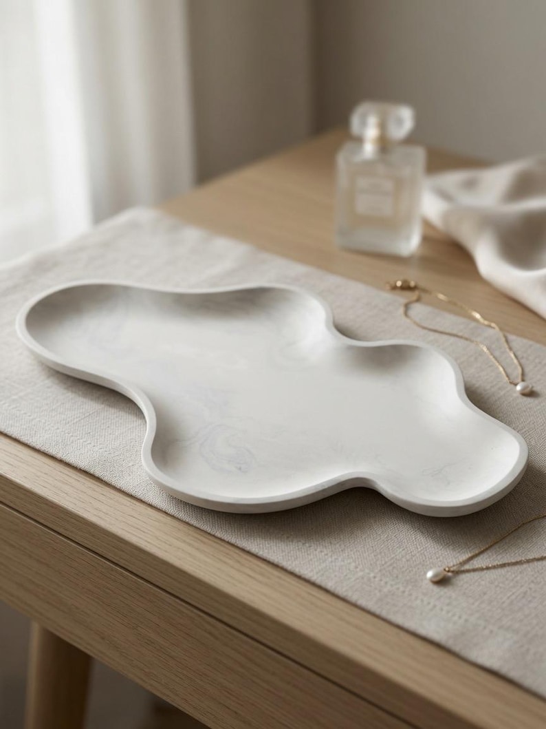 May include: A white tray with a smooth, marbled gray pattern and an irregular, cloud-like organic shape. The tray features a shallow basin with raised edges, crafted from a solid material with a matte finish, designed for holding small items.