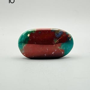 May include: A polished, oval-shaped stone featuring a vibrant colour palette of deep maroon, bright teal, and small patches of blue. The surface is smooth and reflective, displaying natural mineral patterns with distinct colour transitions. Labeled 10.