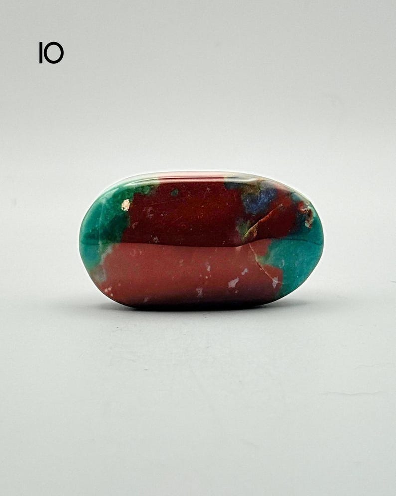 May include: A polished, oval-shaped stone featuring a vibrant colour palette of deep maroon, bright teal, and small patches of blue. The surface is smooth and reflective, displaying natural mineral patterns with distinct colour transitions. Labeled 10.