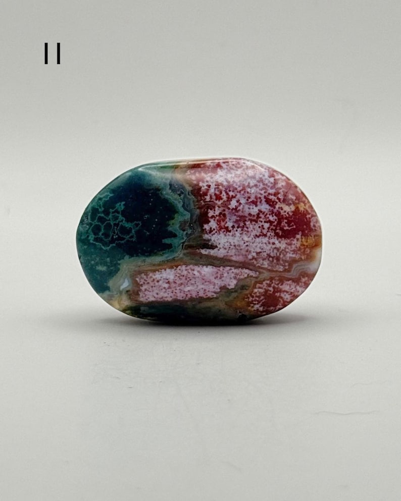 May include: A polished, oval-shaped stone featuring a vibrant mix of deep forest green, bright crimson red, and creamy white patterns. The surface displays intricate, swirling natural inclusions and a smooth, glossy finish throughout the piece.
