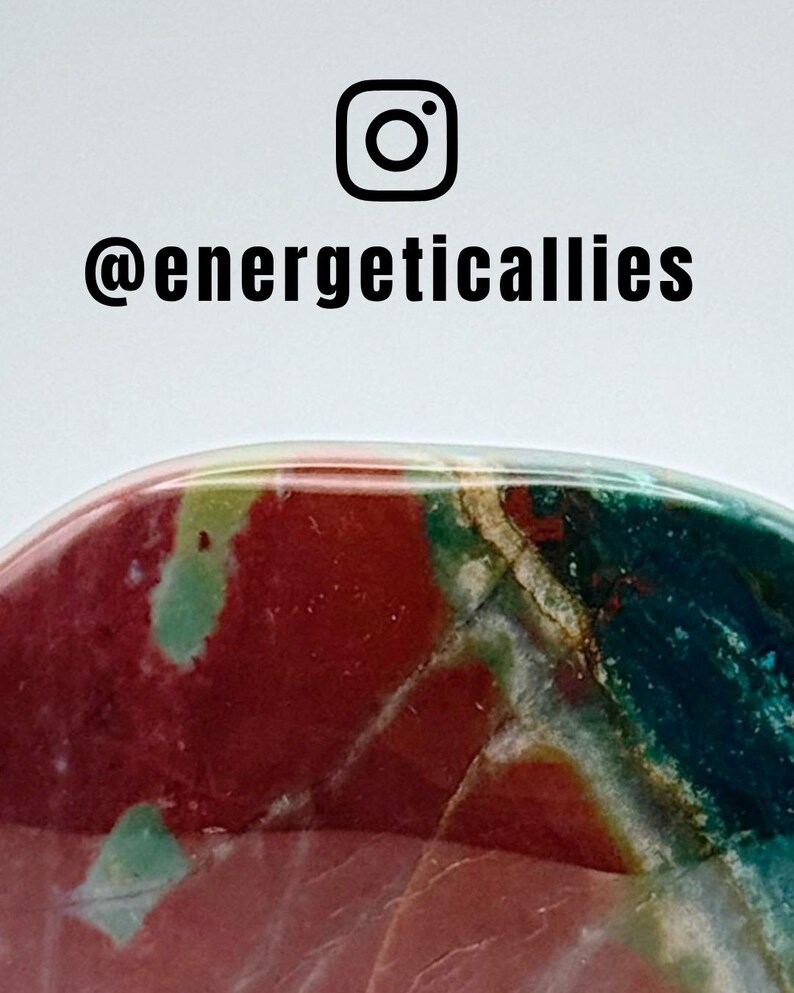 May include: A polished, rounded stone featuring a vibrant mix of deep red, teal, and forest green colours with thin, light-coloured mineral veins running through the surface. Above the stone, the text @energeticallies appears in black.