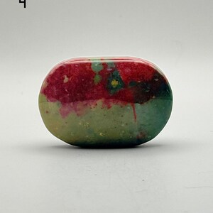 May include: An oval-shaped polished stone featuring a vibrant colour palette of deep magenta, forest green, and olive tones. The surface displays a smooth, glossy texture with natural mottled patterns and distinct colour transitions throughout.
