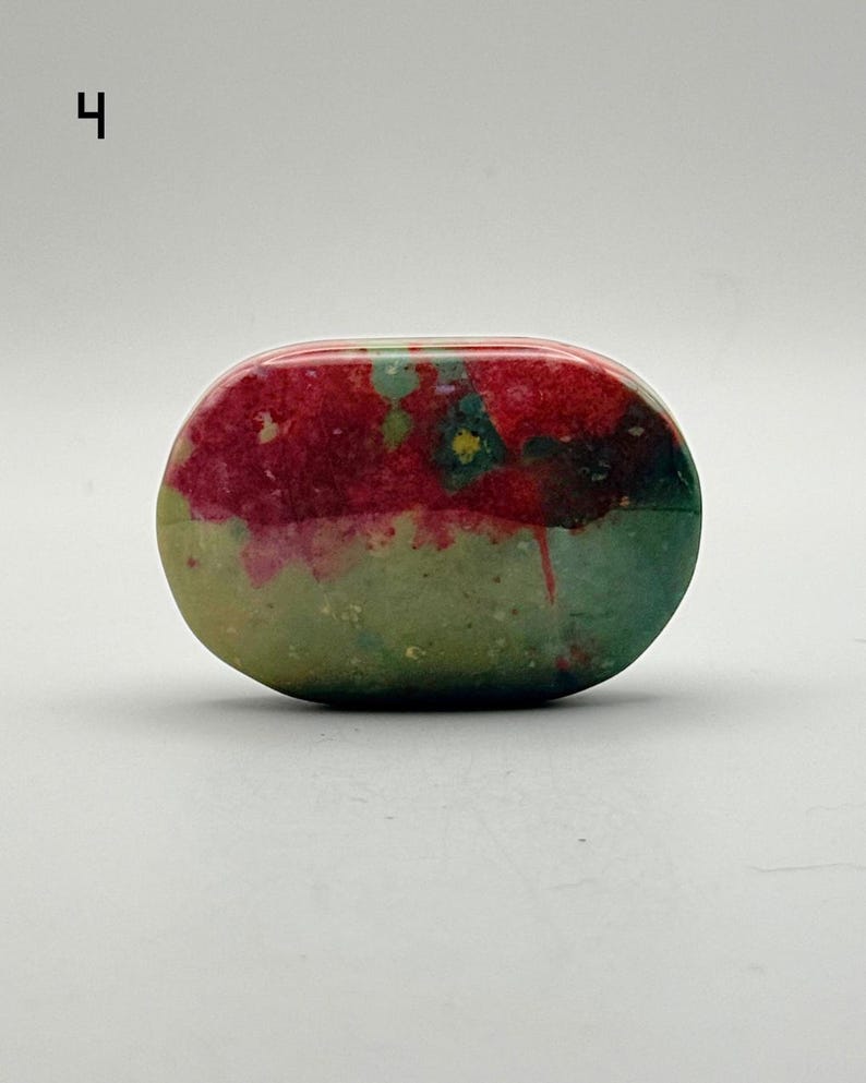 May include: An oval-shaped polished stone featuring a vibrant colour palette of deep magenta, forest green, and olive tones. The surface displays a smooth, glossy texture with natural mottled patterns and distinct colour transitions throughout.