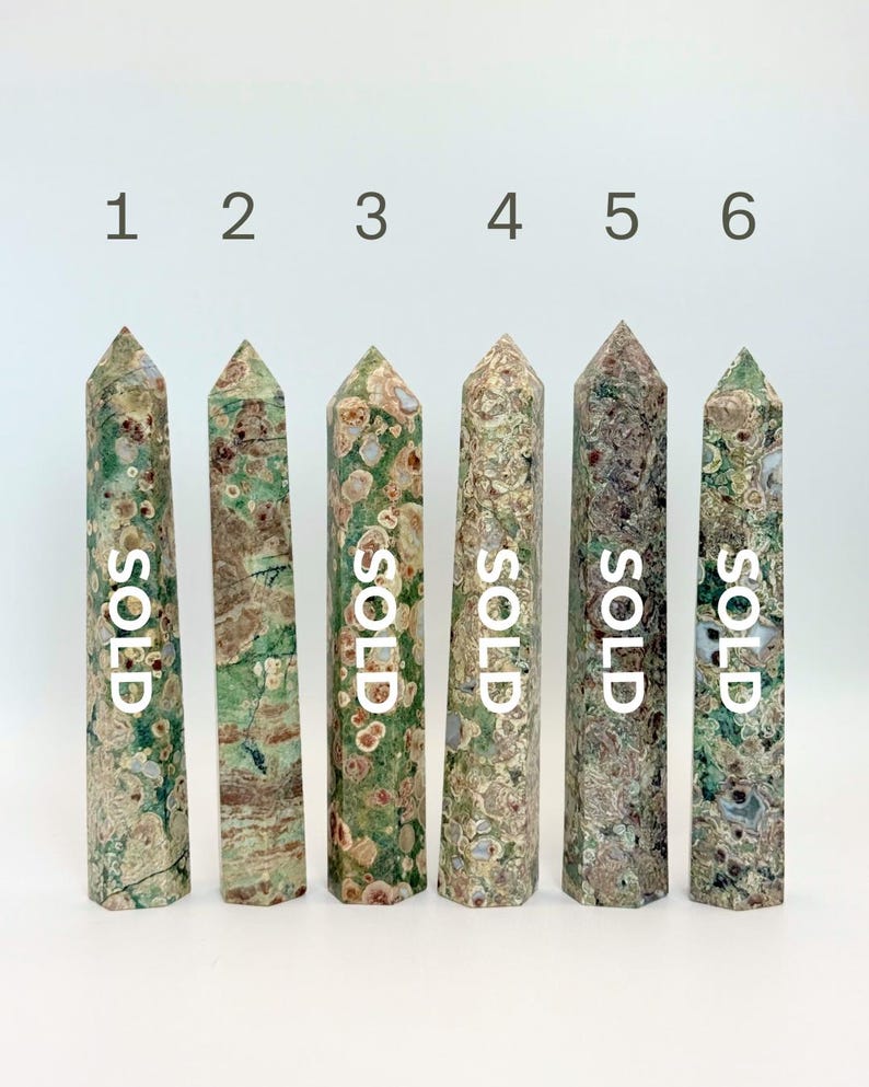 May include: Six tall, pointed crystal towers arranged in a row, numbered one through six. Each stone features a unique mottled pattern of green, brown, and cream colors. The text "SOLD" is printed vertically on five of the six crystal towers.